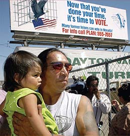 A man holding a baby stands under a sign that reads: "Now that you've done your time, it's time to VOTE. Many former felons can vote in Nevada."