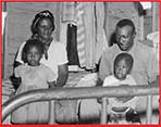 An African American man, woman, and children sitting on a bed. 