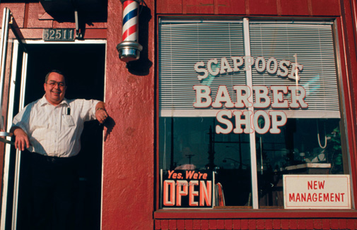 A smiling man stands in the doorway of a barber shop open under new management.