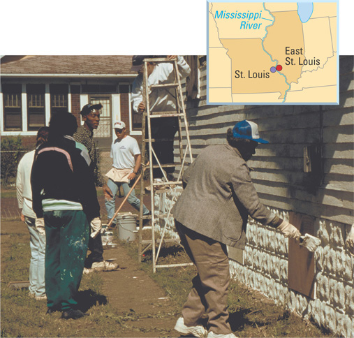 A map of St. Louis, Missouri, and East St. Louis, Illinois, separated by the Mississippi river is in front of a photo of people painting a house as part of a neighborhood revitalization project.