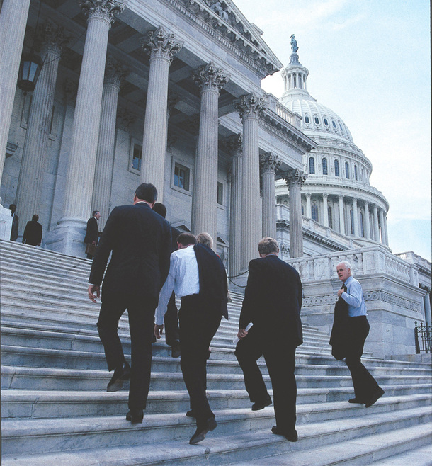 People in suits walk up the steps of the capital building.